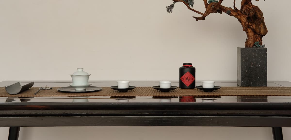 A Chinese tea ceremony set with a gaiwan, cups, and a bonsai tree on a dark wood table