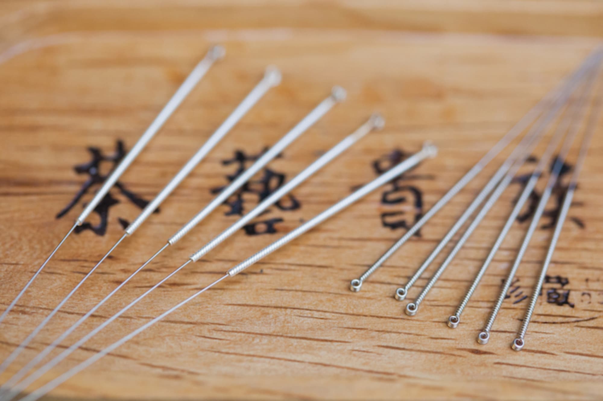 Acupuncture needles laid out on a wooden table marked with Chinese characters
